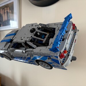 May include: A gray and blue model car made of interlocking plastic bricks. The car has a large blue spoiler and blue and white accents. The model is mounted on a wall. The text "JASFDesign" is visible on the side.