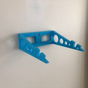 May include: A light blue wall-mounted bracket with the text "APOLLO" and "LRV". The bracket has a series of circular cutouts and is secured to a white wall with a screw. The text "JASFDesign" is also visible.