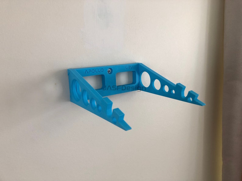 May include: A light blue wall-mounted bracket with the text "APOLLO" and "LRV". The bracket has a series of circular cutouts and is secured to a white wall with a screw. The text "JASFDesign" is also visible.