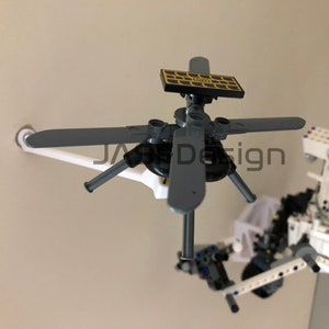 May include: A close-up of a small, gray, Lego helicopter with four blades and a solar panel on top. The helicopter is attached to a white Lego base.