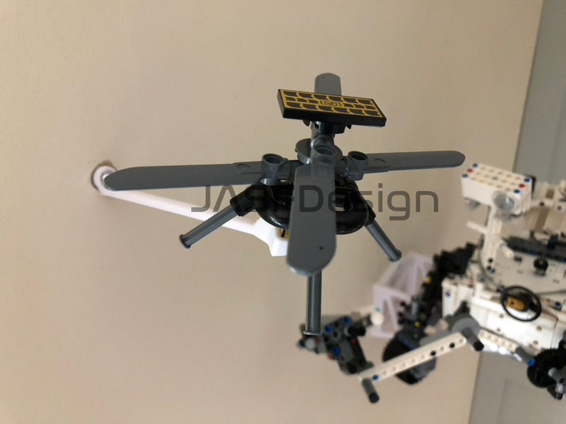 May include: A close-up of a small, gray, Lego helicopter with four blades and a solar panel on top. The helicopter is attached to a white Lego base.