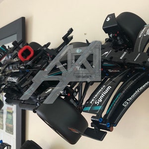 May include: A black Lego model of a Formula 1 race car with Petronas and Syntium branding. The car is mounted on a wall and has a red detail on the rear wing.