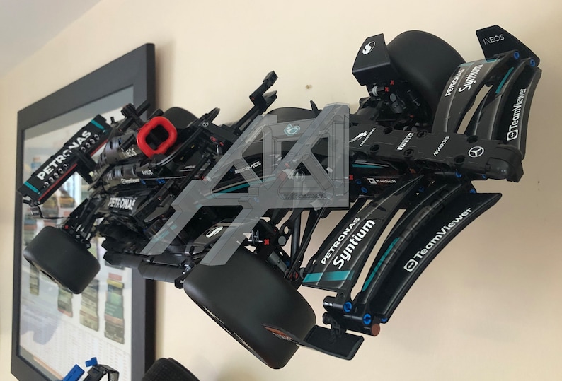 May include: A black Lego model of a Formula 1 race car with Petronas and Syntium branding. The car is mounted on a wall and has a red detail on the rear wing.