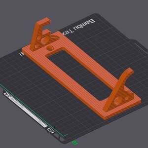 May include: A 3D printed orange-brown phone stand with a rectangular base and two angled supports. The stand is designed to hold a phone upright. The stand is printed on a black textured surface with a grid pattern. The text "Bambu Lab" is printed on the surface.
