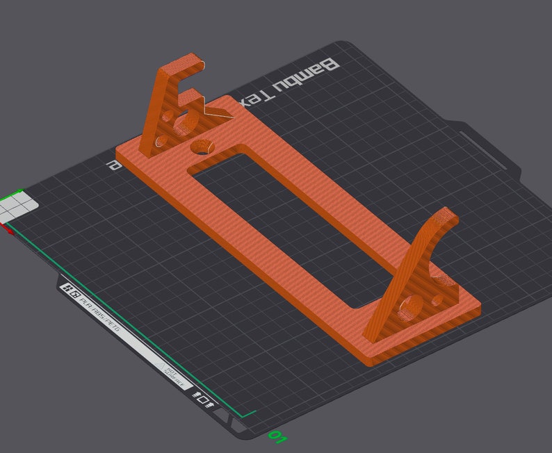 May include: A 3D printed orange-brown phone stand with a rectangular base and two angled supports. The stand is designed to hold a phone upright. The stand is printed on a black textured surface with a grid pattern. The text "Bambu Lab" is printed on the surface.