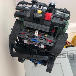 May include: A black and green Lego model of a truck with a detailed engine and suspension. The truck is upside down and the underside is visible.