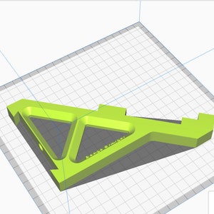 K&ouml;nnte beinhalten: Ein dreieckiges Objekt aus limegr&uuml;nem, 3D-gedrucktem Kunststoff mit einem Loch in der Mitte und einem kleinen Text auf der Oberfl&auml;che. Das Objekt befindet sich auf einem wei&szlig;en Gitterhintergrund.