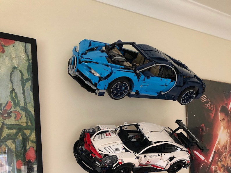 May include: Two Lego model cars displayed on a wall. The top car is a blue Bugatti Chiron, and the bottom car is a white Porsche 911 GT3 RS.
