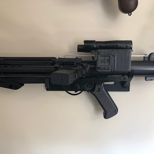 May include: A black plastic toy blaster with a scope and a handle. The blaster has a textured surface and a silver trigger.