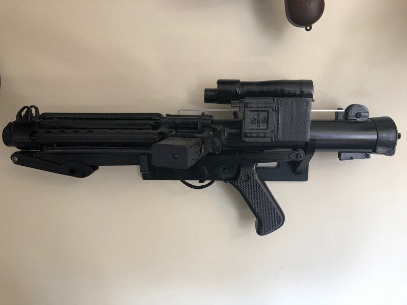 May include: A black plastic toy blaster with a scope and a handle. The blaster has a textured surface and a silver trigger.