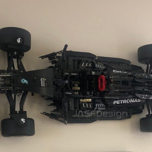 May include: A black and green Lego Formula 1 race car model with Petronas branding. The car is on a white surface and is missing some parts.