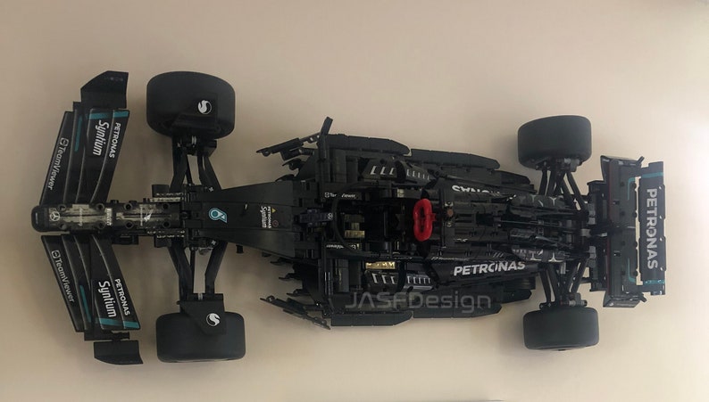 May include: A black and green Lego Formula 1 race car model with Petronas branding. The car is on a white surface and is missing some parts.
