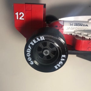 Op de afbeelding: Een rood en wit model van een raceauto met het nummer 12 aan de zijkant. De zwarte band heeft de woorden "GOOD YEAR EAGLE" in het wit. De auto is voorzien van de tekst "POWERED BY HONDA" en "JASFDesign".