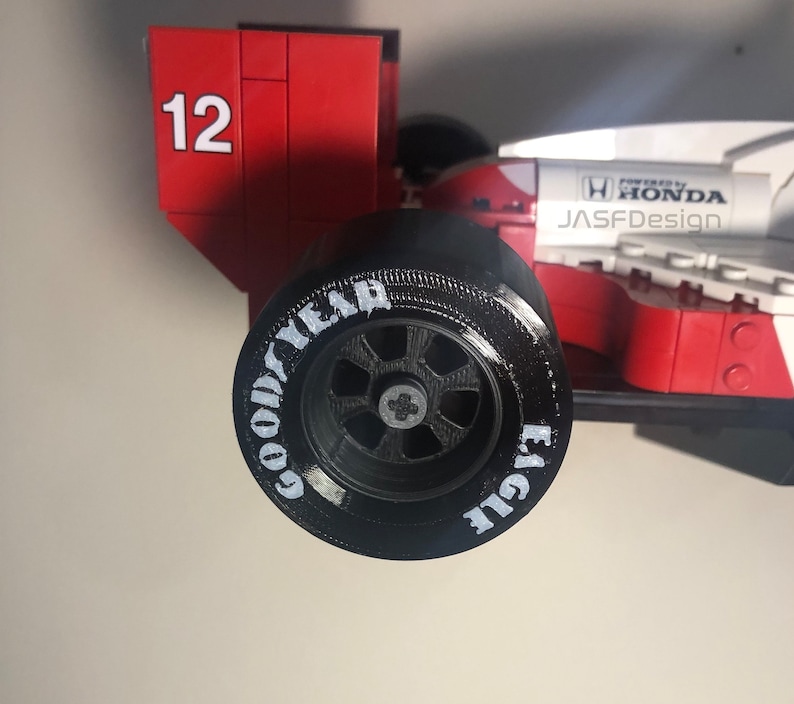 Op de afbeelding: Een rood en wit model van een raceauto met het nummer 12 aan de zijkant. De zwarte band heeft de woorden "GOOD YEAR EAGLE" in het wit. De auto is voorzien van de tekst "POWERED BY HONDA" en "JASFDesign".