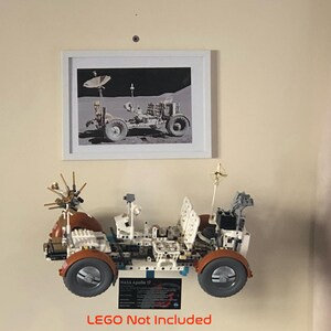 May include: A framed black and white photograph of a lunar rover is displayed above a detailed model of a lunar rover. The model has orange wheels and is labeled "NASA Apollo 17". The text "LEGO Not Included" is at the bottom.