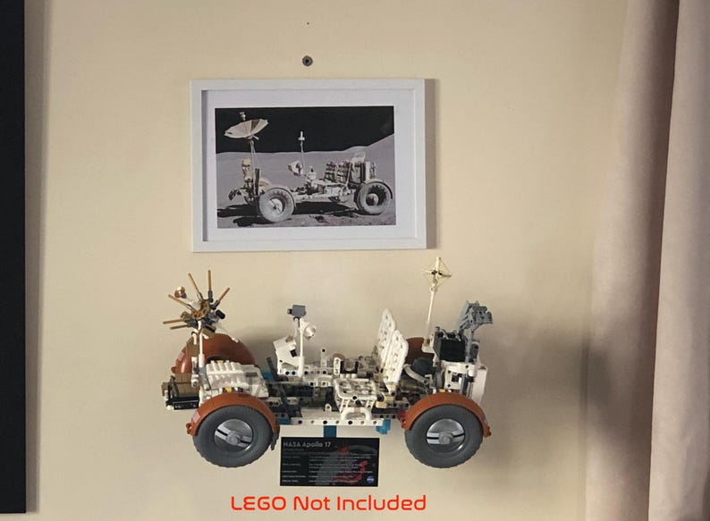 May include: A framed black and white photograph of a lunar rover is displayed above a detailed model of a lunar rover. The model has orange wheels and is labeled "NASA Apollo 17". The text "LEGO Not Included" is at the bottom.