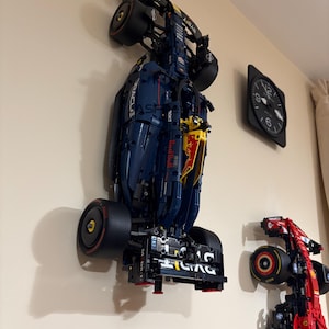 May include: Two Lego Formula 1 race cars mounted on a wall. The blue and yellow car is a Red Bull Racing car with the Oracle logo. The red car is a Ferrari car.