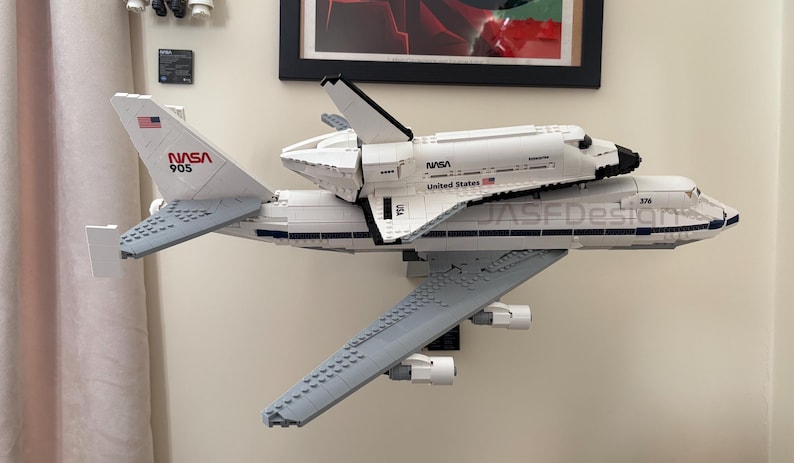 May include: A white LEGO model of a NASA space shuttle atop a Boeing 747 aircraft. The model features the NASA logo and the text "United States". The aircraft has the text "JASEDesign" on the side.