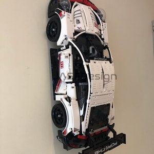 May include: A white and black Lego Porsche 911 GT3 RS model car with red accents. The car is mounted on a wall with a black spoiler and the text "PORSCHE" on the back.