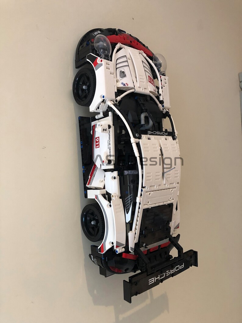 May include: A white and black Lego Porsche 911 GT3 RS model car with red accents. The car is mounted on a wall with a black spoiler and the text "PORSCHE" on the back.