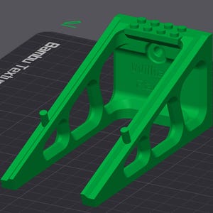 May include: A bright green 3D-printed object with a geometric design. The object has a rectangular top with circular pegs and a support structure with angled supports. The text "Willie" and "FB" are visible on the side.