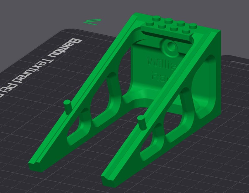 May include: A bright green 3D-printed object with a geometric design. The object has a rectangular top with circular pegs and a support structure with angled supports. The text "Willie" and "FB" are visible on the side.