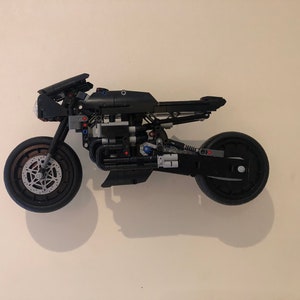 May include: A black Lego motorcycle model with detailed engine and wheels. The motorcycle is mounted on a white wall.