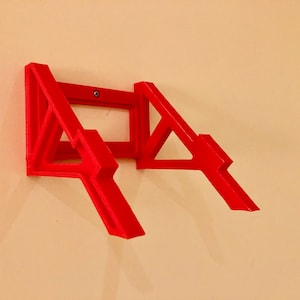 May include: A red plastic wall mount for a laptop or tablet. The mount is designed to hold the device at an angle, allowing for easy viewing.