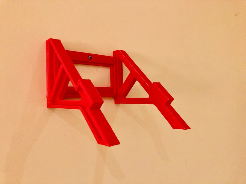 May include: A red plastic wall mount for a laptop or tablet. The mount is designed to hold the device at an angle, allowing for easy viewing.