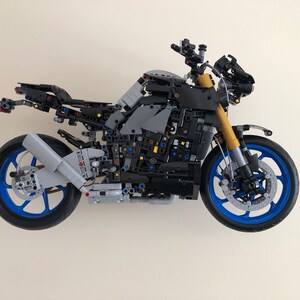 Peut inclure: Un mod&egrave;le de moto Lego noir et gris avec des roues bleues et un moteur d&eacute;taill&eacute;. La moto est construite avec de nombreuses petites pi&egrave;ces et a un design r&eacute;aliste.