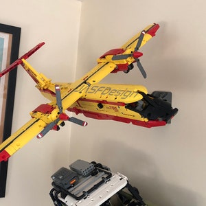 Op de afbeelding: Een geel en rood Lego-vliegtuigmodel met zwarte details. Het model is gelabeld met "JASFDesign" en "FIRE 301".