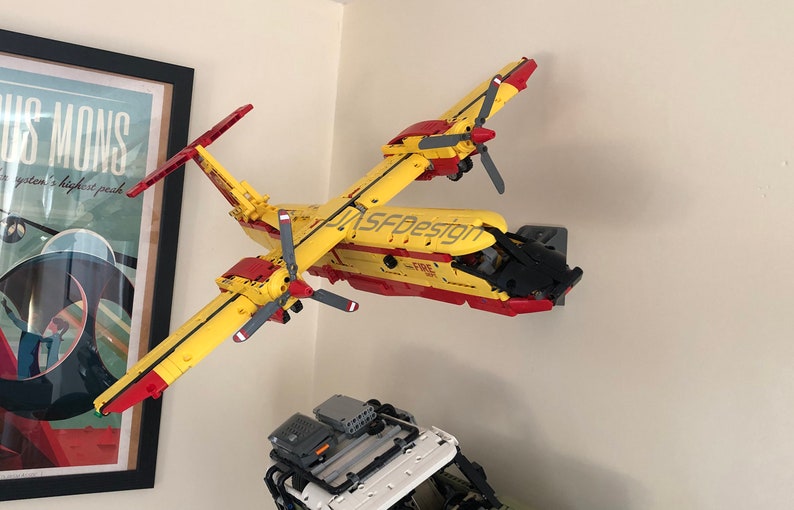 Op de afbeelding: Een geel en rood Lego-vliegtuigmodel met zwarte details. Het model is gelabeld met "JASFDesign" en "FIRE 301".