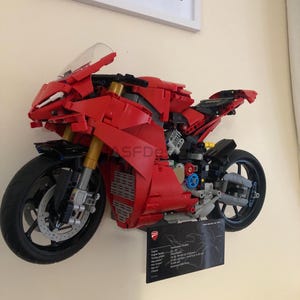 May include: A red and black Lego Ducati Panigale V4 R motorcycle model. The model is displayed on a wall with a black plaque containing technical specifications for the real motorcycle.