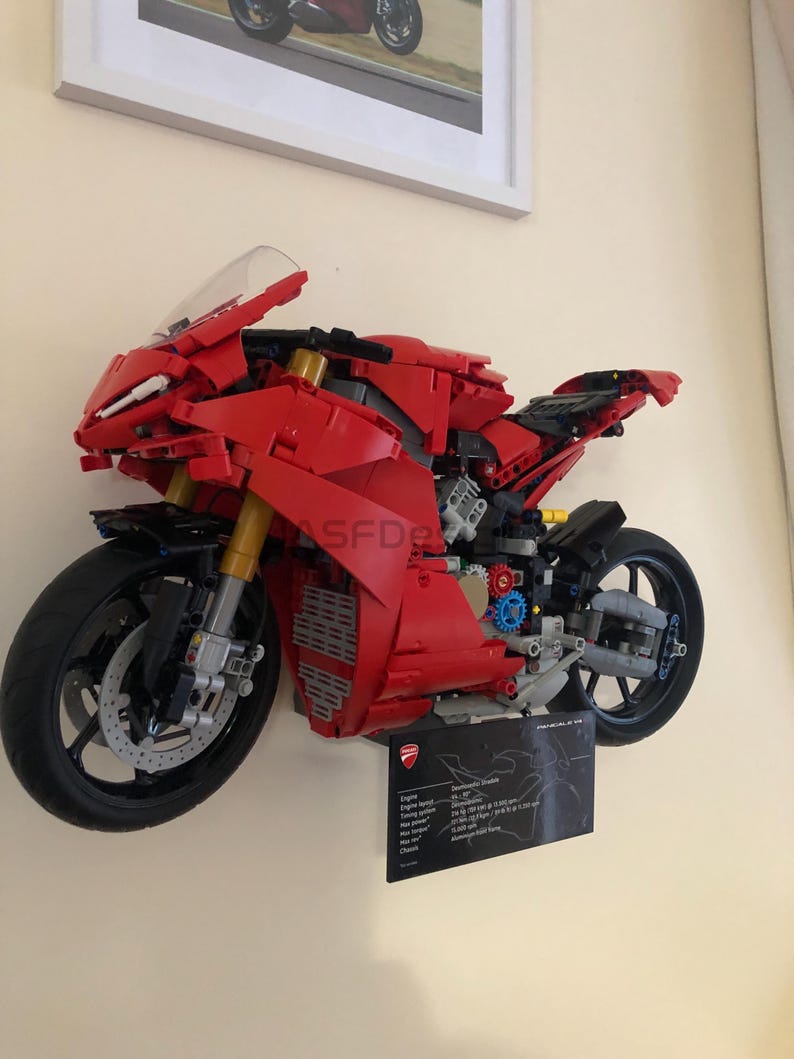May include: A red and black Lego Ducati Panigale V4 R motorcycle model. The model is displayed on a wall with a black plaque containing technical specifications for the real motorcycle.