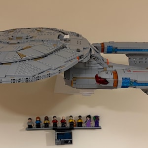 Puede incluir: Un gran modelo Lego gris de la nave espacial Star Trek USS Enterprise. El modelo est&aacute; montado en una pared, con una peque&ntilde;a exhibici&oacute;n de figuras de Lego debajo. La nave presenta una construcci&oacute;n y un dise&ntilde;o detallados.