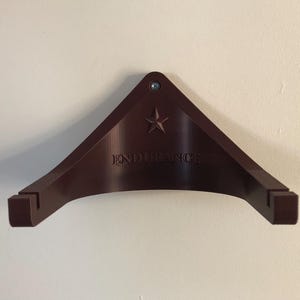 May include: A dark brown wall mount with a star and the word "ENDURANCE" printed on it. The mount is designed to hold a guitar.