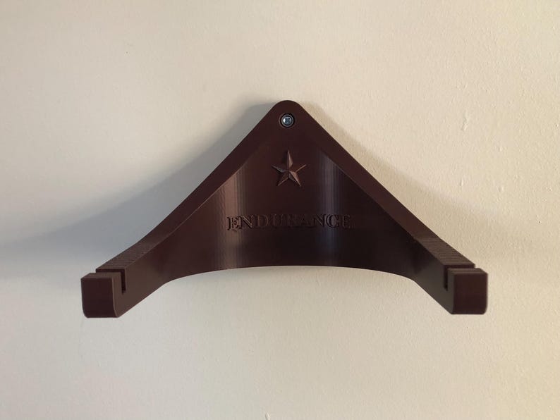 May include: A dark brown wall mount with a star and the word "ENDURANCE" printed on it. The mount is designed to hold a guitar.