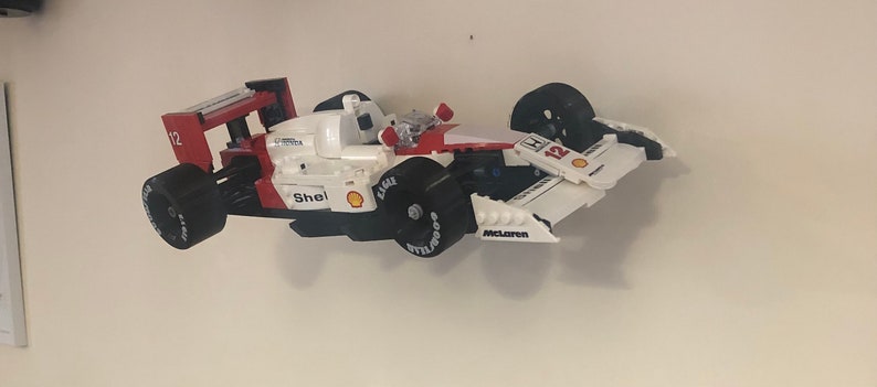 May include: A red, white, and black Lego model of a Formula One race car. The car has the number 12 on the side and the word "McLaren" on the bottom. The car is made of plastic and has a detailed design.