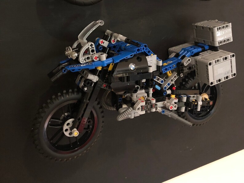 May include: A blue and black Lego motorcycle model with a BMW logo on the side. The motorcycle has two side cases and a top case. The motorcycle is on a black background.