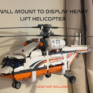 May include: White and orange Lego helicopter with black blades and a white and black "Heavy-Lift Service" sticker. The helicopter is mounted on a white wall mount with the text "WALL MOUNT TO DISPLAY HEAVY LIFT HELICOPTER" and "LEGO NOT INCLUDED" printed below.