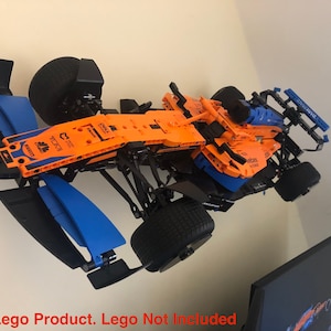 May include: A black and orange Lego Formula 1 race car model with blue accents. The car is mounted on a wall and has a black and blue wing on each side. The car has the text "DELL" and "McLaren" on it.
