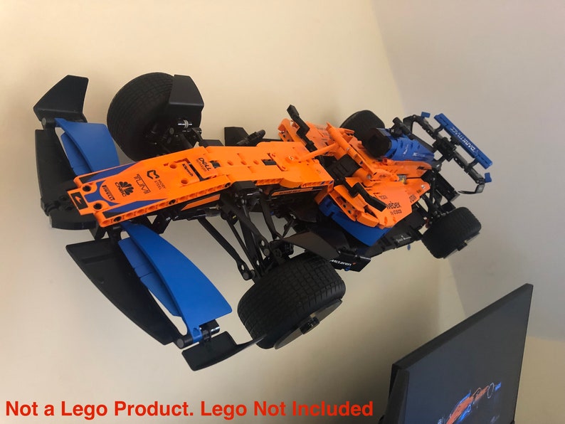 May include: A black and orange Lego Formula 1 race car model with blue accents. The car is mounted on a wall and has a black and blue wing on each side. The car has the text "DELL" and "McLaren" on it.