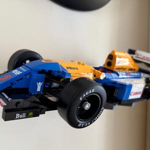 May include: A blue, yellow, and white race car model with black tires. The model has the words "elf", "Williams", and "Canon" printed on it. The tires have the word "Eagle" printed on them.