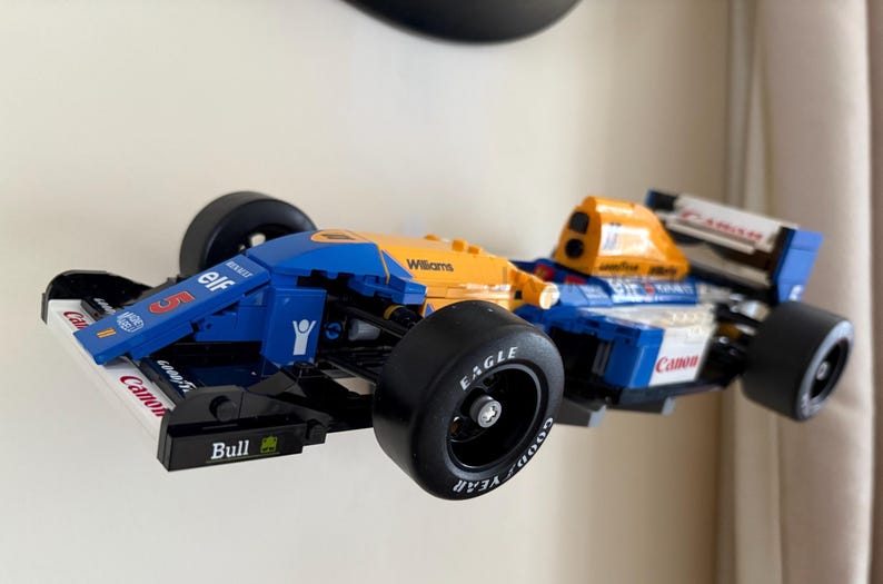 May include: A blue, yellow, and white race car model with black tires. The model has the words "elf", "Williams", and "Canon" printed on it. The tires have the word "Eagle" printed on them.