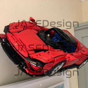 May include: A red Lego Ferrari model car with black accents and a blue interior. The car is mounted on a wall and appears to be floating.