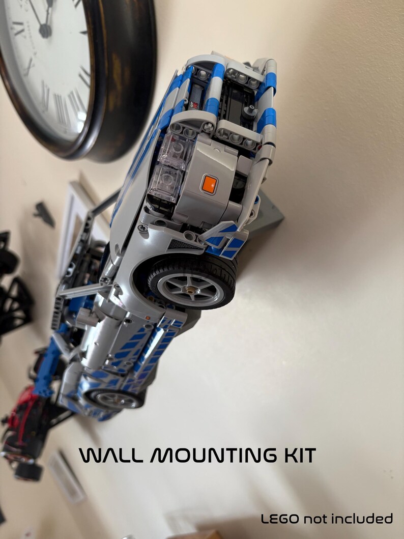 May include: A silver and blue toy car mounted on a wall, with the text "WALL MOUNTING KIT" below. The car has visible wheels and detailed features. A clock is visible in the background.
