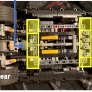 K&ouml;nnte beinhalten: Nahaufnahme der Unterseite eines schwarzen Lego Technic Automodells. Das Auto hat zwei gelbe Achsen und schwarze Zahnr&auml;der. Die Hinterr&auml;der sind links und die Vorderr&auml;der rechts sichtbar.