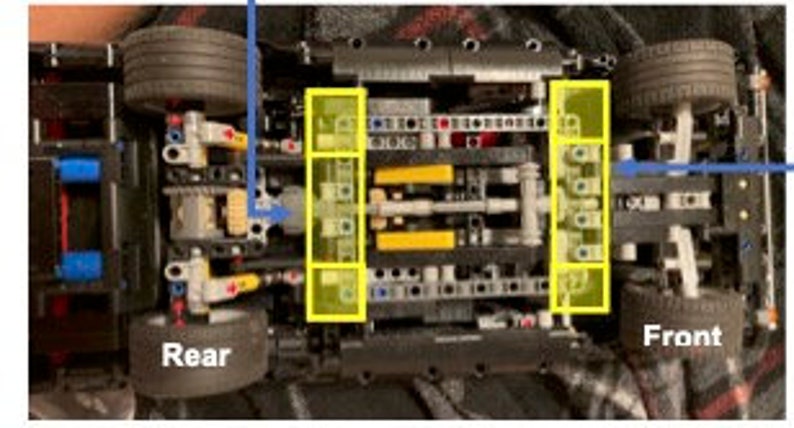 K&ouml;nnte beinhalten: Nahaufnahme der Unterseite eines schwarzen Lego Technic Automodells. Das Auto hat zwei gelbe Achsen und schwarze Zahnr&auml;der. Die Hinterr&auml;der sind links und die Vorderr&auml;der rechts sichtbar.