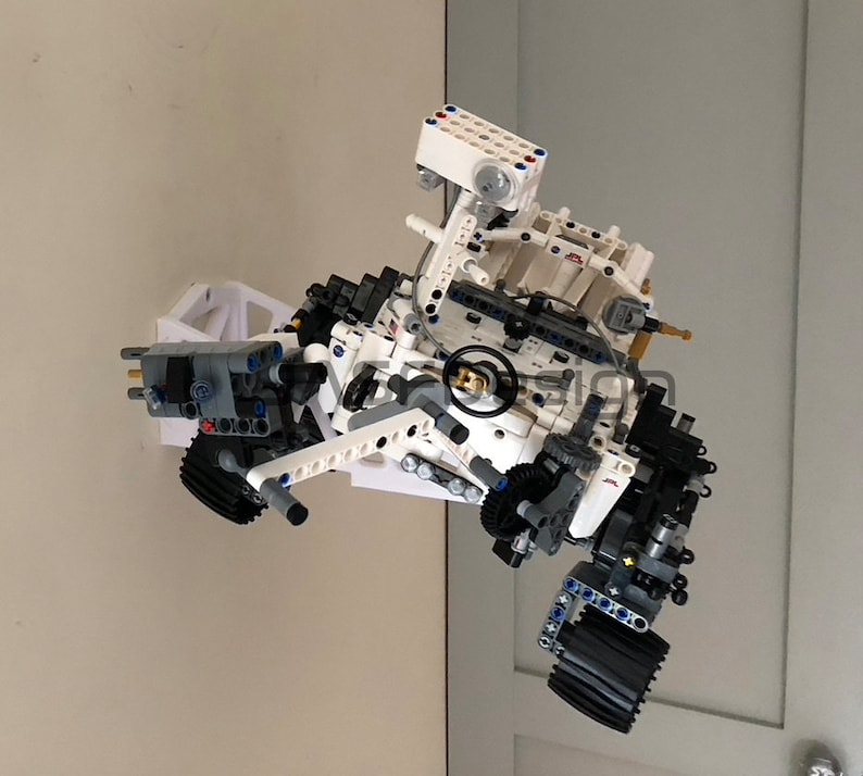 May include: A white and gray Lego model of the Mars rover Curiosity. The rover has six wheels, a robotic arm, and a camera. The model is detailed and realistic.