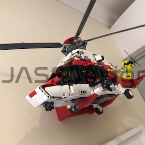May include: A red, white, and black Lego helicopter model with a yellow rotor blade. The helicopter is mounted on a wall.